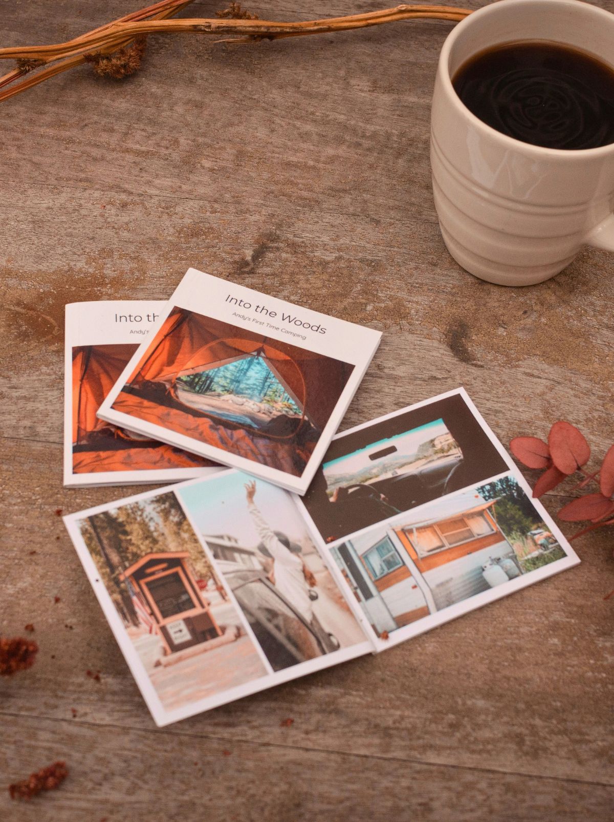 Two closed and one open mini photo book of a camping trip, on a wooden table beside a mug of coffee